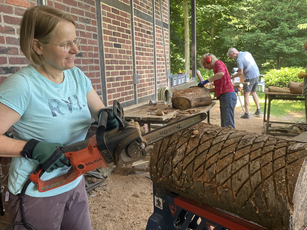Teilnehmerin formt mit der Kettensäge einen Holzstamm